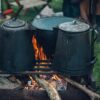 Camp kettles and pot over open fire at an outdoor campsite, ideal for rustic cooking themes.